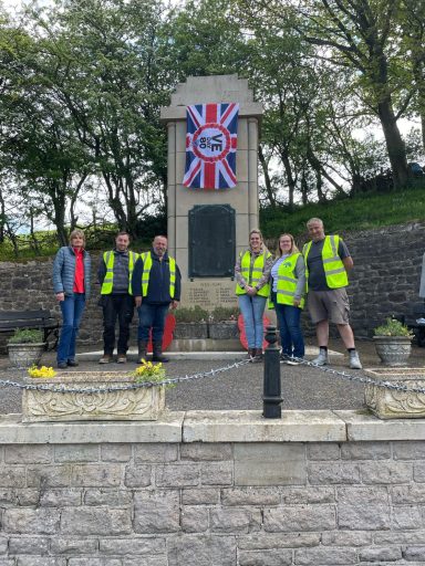 Group of people in high-visibility vests near a memorial, with a Union Jack banner.