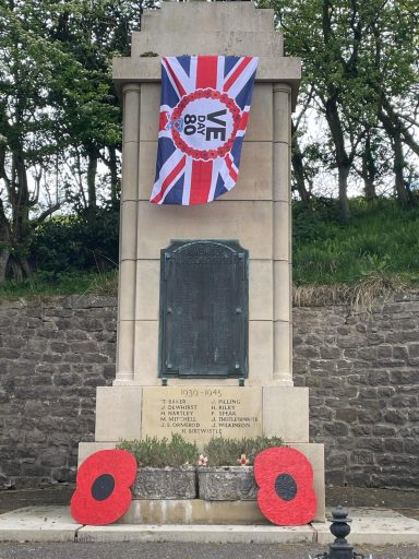A war memorial with a Union Jack flag and red poppy wreaths at the base.