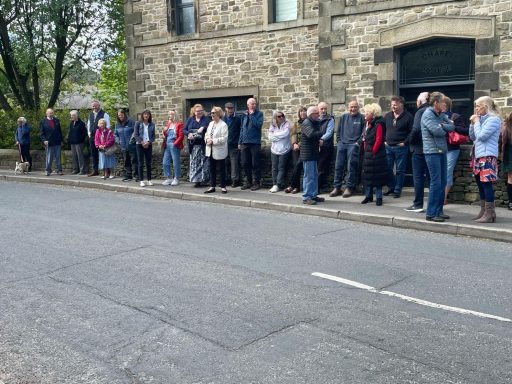 A queue of people lined up along a stone building on a street.