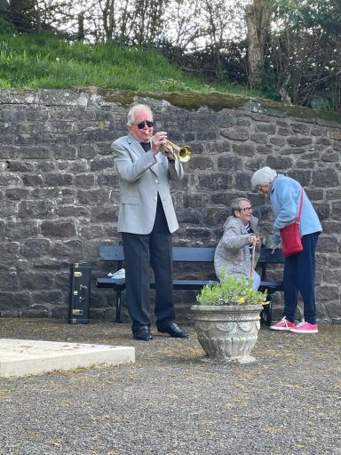 A man in a suit plays trumpet while an elderly couple engages nearby.