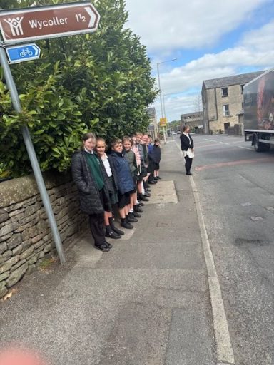 A group of people in formal attire standing by a roadside near a signpost.